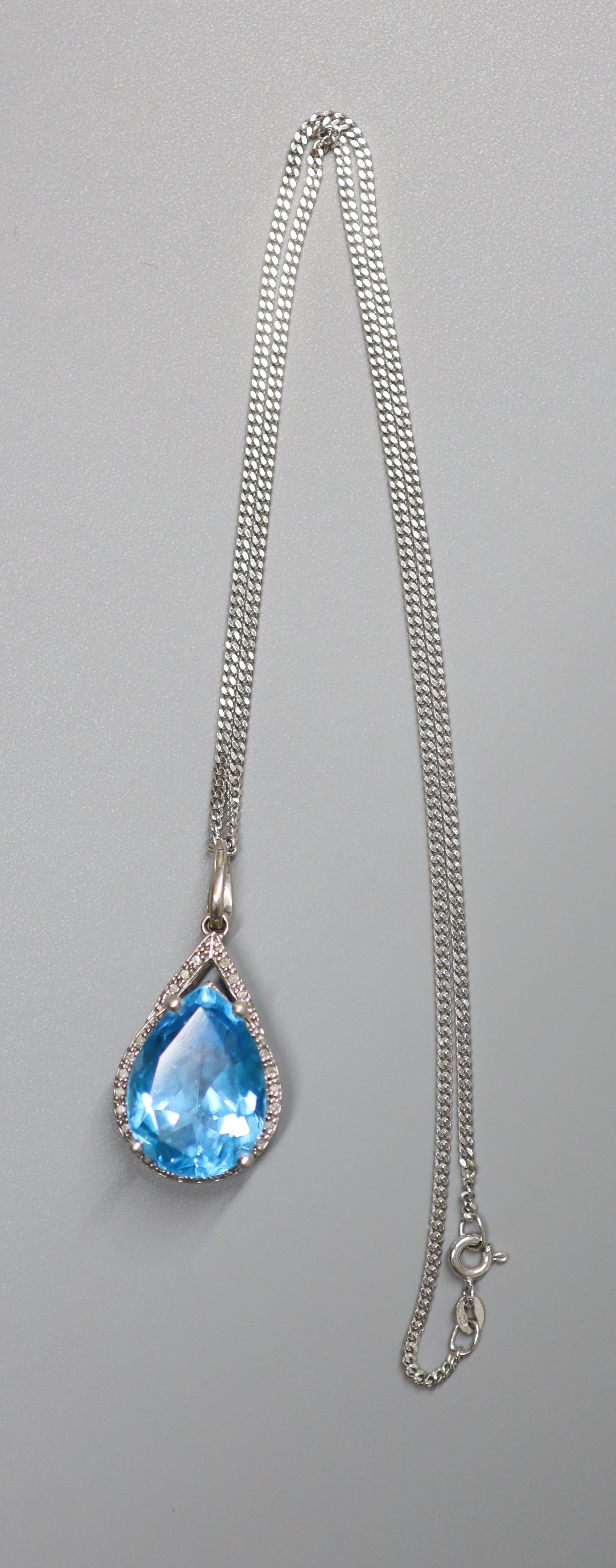 A modern white metal (stamped 9k), blue topaz and diamond chip set pendant, 29mm, on a 9ct white gold chain, 44cm, gross weight 12.3 grams